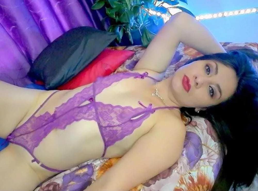 NicoletteWet lays in her purple lingerie on her back facing the camera