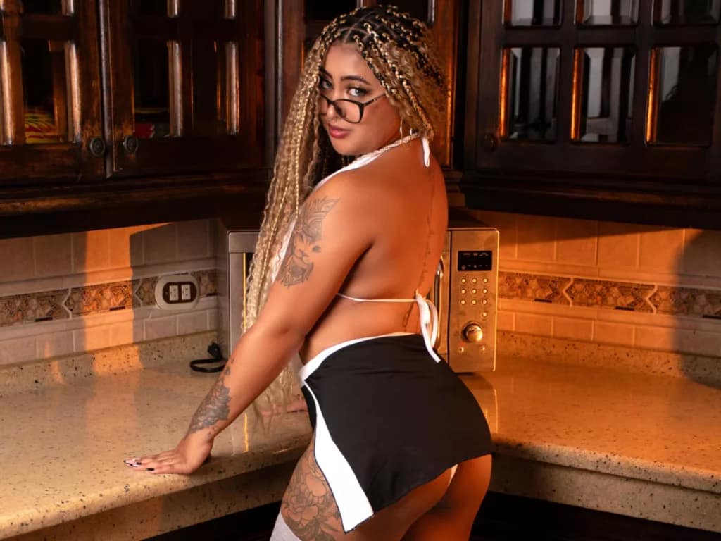 BBW ebony Latina LuisaCameron in white bikini top, leaning on kitchen counter.